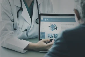 Gambar seorang dokter sedang mengarahkan tampilan website kepada pasien untuk memberikan informasi layanan kesehatan secara digital. - Mentor Juara 